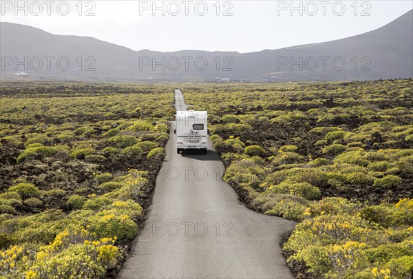 Motorhome on straight sealed tarmac road crossing lava flows Malpais de Corona, Lanzarote, Canary