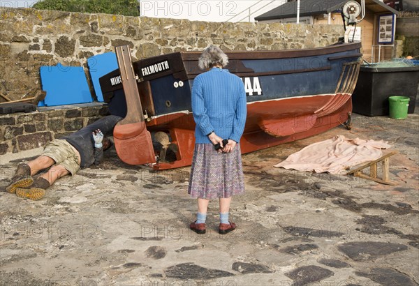 Man painting small fishing boat watched by an elderly woman presumably his mother, Coverack,