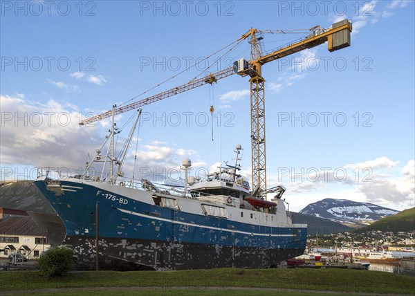 Construction crane towering above fishing boat boat in dry dock, Tromso, Norway, Europe