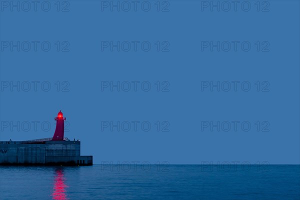 Red lighthouse on end of concrete pier after sunset in Jeju, South Korea, Asia