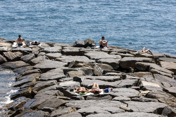 Tourists sunbathe on a stone groyne jutting out into the sea, Imperia, 01.06.2022