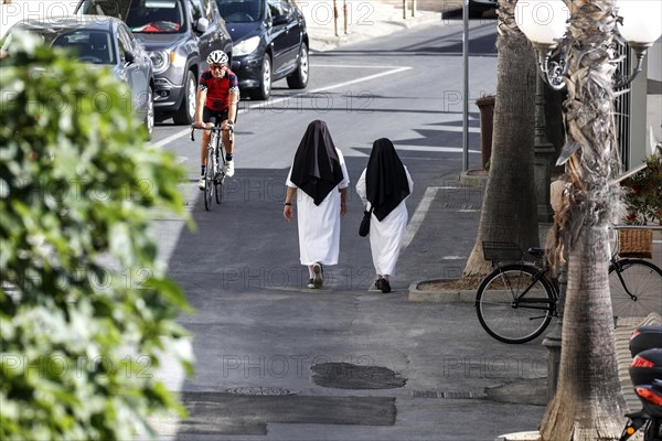 Two nuns walk across a street in Diana Marina, a man on a racing bike rides past, 28/05/2022