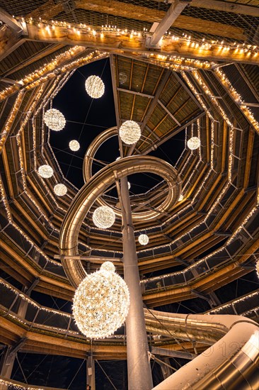 Spiral structure with fairy lights viewed from below, enchanting forest dwellers, treetop walk Bad