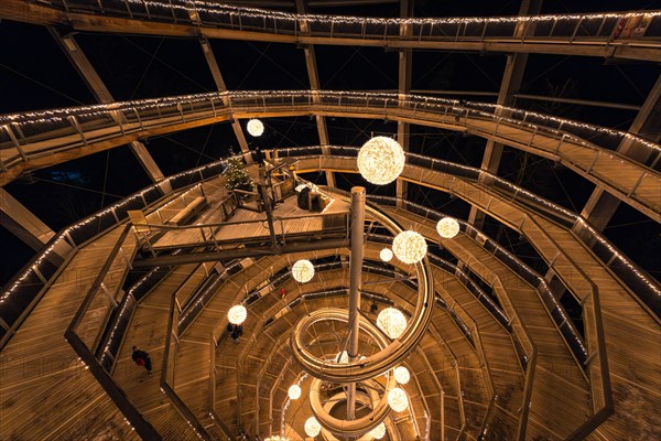 People walk through a spiral-shaped wooden construction with lights at night, magical forest