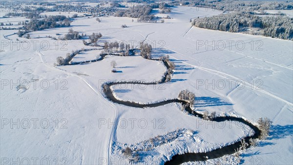 Drone shot of the river Schmutter meandering naturally through the snowy winter landscape of the