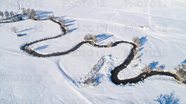 Drone shot of the river Schmutter meandering naturally through the snowy winter landscape of the