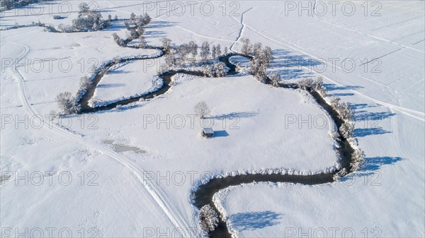 Drone shot of the river Schmutter meandering naturally through the snowy winter landscape of the