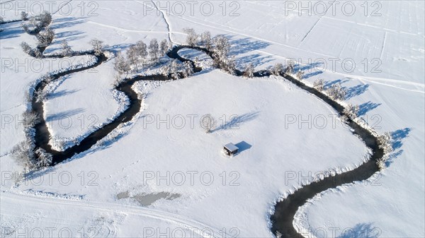 Drone shot of the river Schmutter meandering naturally through the snowy winter landscape of the
