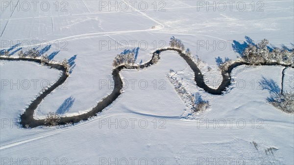 Drone shot of the river Schmutter meandering naturally through the snowy winter landscape of the