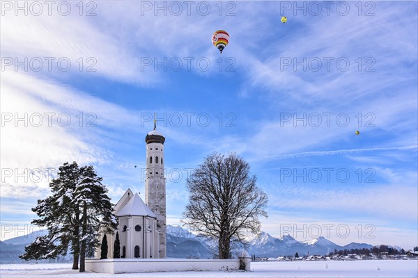 Hot air balloon over the pilgrimage church of St Coloman near Schwangau in winter, Allgäu, Swabia,