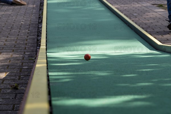 Red ball rolls on green minigolf course, Germany, Europe