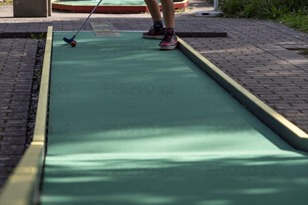Boy hits ball on green minigolf course