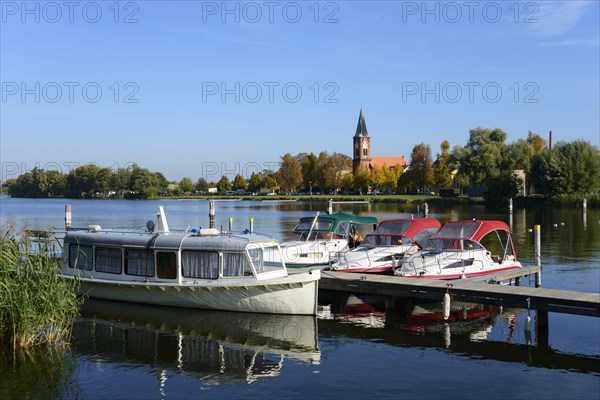 Boats lying on a calm lake in front of a church surrounded by trees under a clear blue sky, ships,