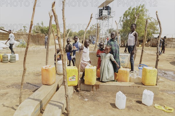 Children and adults stand with water canisters at a well in the Gorom refugee settlement southwest
