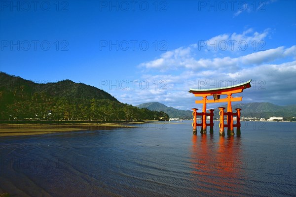 The bright red Sea-gate of Miyajima temple, Japan, against a background of sea and the low hills
