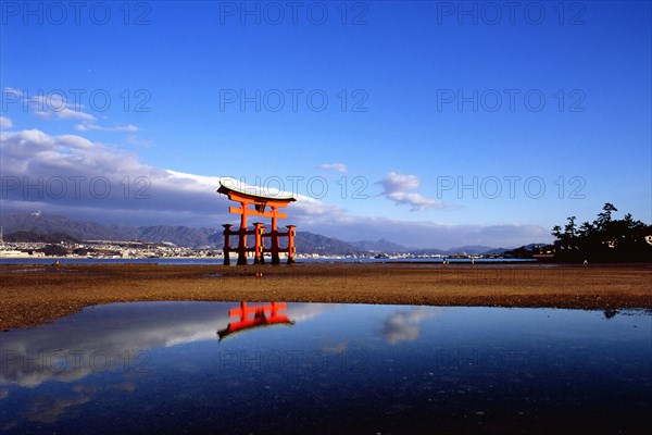The bright red Sea-gate of Miyajima temple, Japan, against a background of sea and the low hills