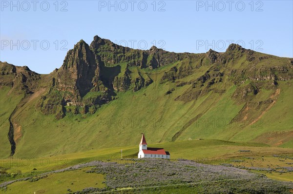 Small red and white church on a hilltop, surrounded by crags and steep hillsides, above the town of