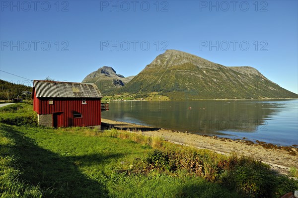 Red wooden boathouse at Lia with the island of Aldra and the Hjarttinden peaks behind, north-west