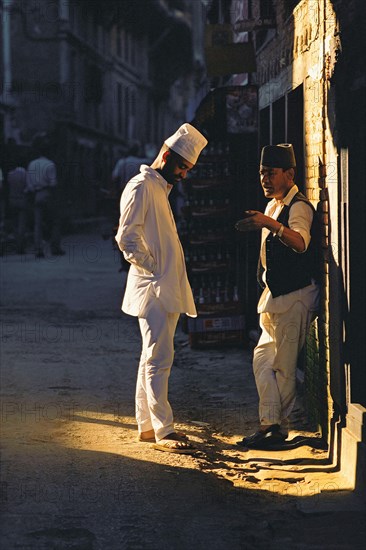 Two men chat in a patch of sunlight in a Kathmandu backstreet, Kathmandu, Nepal, Asia