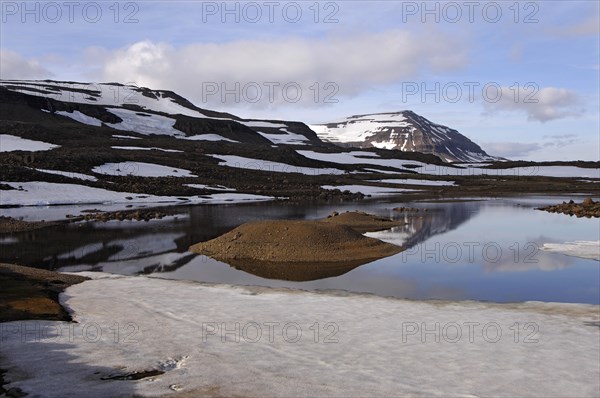 Still partly-frozen meltwater pool and the mountain Bjolfur in the Fjardarheidi range near