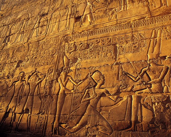 Elaborate carved stone relief with close-ups of pharonic figures in strong evening side-light, at