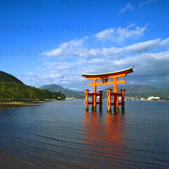 The bright red Sea-gate of Miyajima temple, Japan, against a background of sea and the low hills