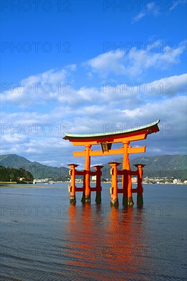 The bright red Sea-gate of Miyajima temple, Japan, against a background of sea and the low hills