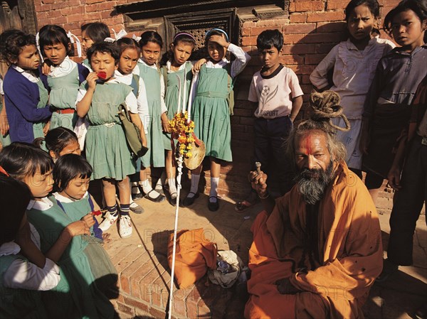 A group of young schoolgirls gathers round fascinated by a Hindu holy man or saddhu outside the