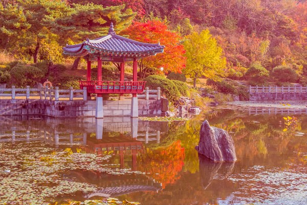 Oriental gazebo with terracotta tile roof at edge of man made pond in local public park in South