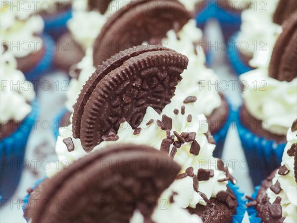 Close-up of a large group chocolate cupcakes with white cream frosting, dark chocolate cookie