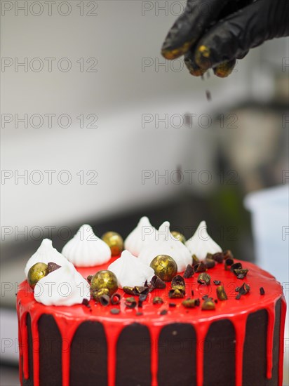 Chef sprinkling gold dust chocolate over a frosted dripping red brown dark chocolate cake with