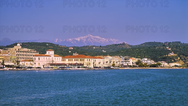 Coastal city view with buildings in front of a mountain backdrop under a clear blue sky,