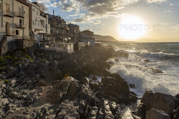 Sea water crashes against the cliffs of the rugged coastline in the town of Cefalu, Sicily, Italy,