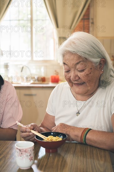 Portrait of an elderly Japanese woman with gray hair eating rice with chopsticks. Vertical portrait
