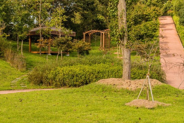 Landscape of urban park with covered gazebo, wooden trellises and concrete hiking trail in South