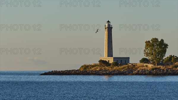 Lighthouse on the coast at dusk with a flying bird in the background, Gythio, Mani, Peloponnese,