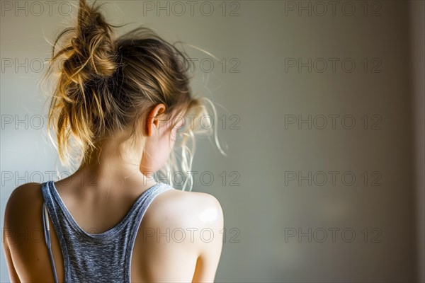 Back view of a girl in soft light, her hair tied into a loose bun, symbolising depression and