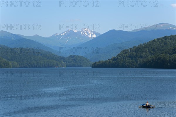 A small boat on a calm blue reservoir with snow-capped mountains in the background, Vidraru
