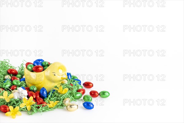 Chocolate eggs and a decorative chick surrounded by artificial grass as a festive decoration, white