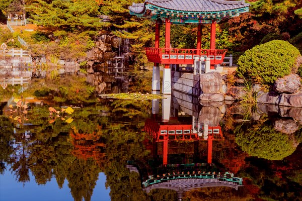 Beautiful oriental gazebo with terracotta tile roof at edge of man made pond with small waterfall