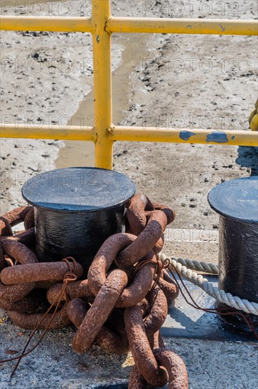 Rusty chain wrapped around ships mooring post in front of yellow metal fence in Yeosu, South Korea,