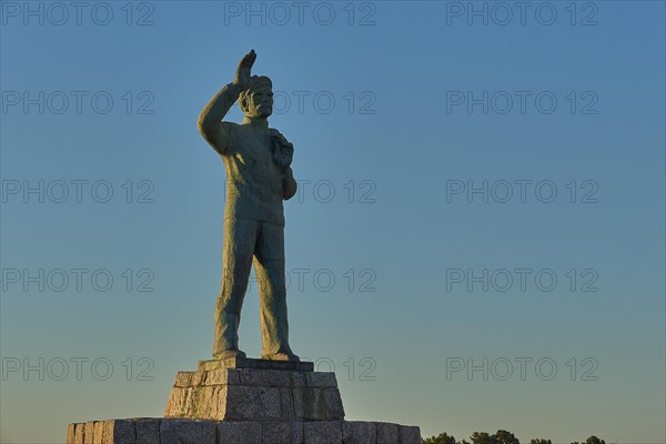 Statue of a man with his arm outstretched towards the sky at dawn, bronze statue of a waving sailor