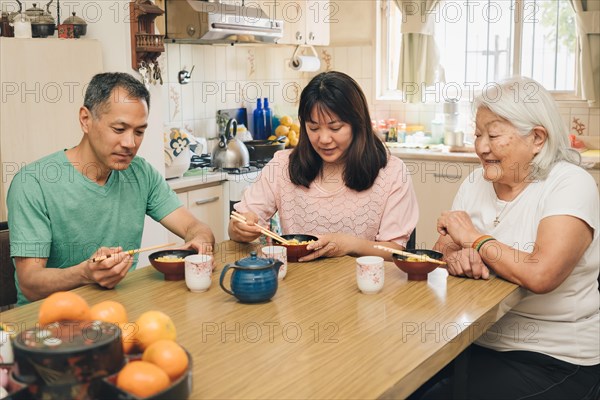 Japanese adult family eating rice with chopsticks. White-haired elderly mother enjoys watching her