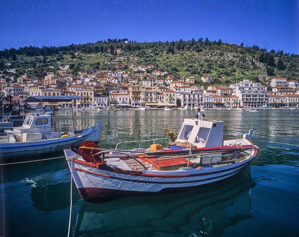 Small boats in the calm harbour water with mountain and city view in the background, Gythio, Mani,