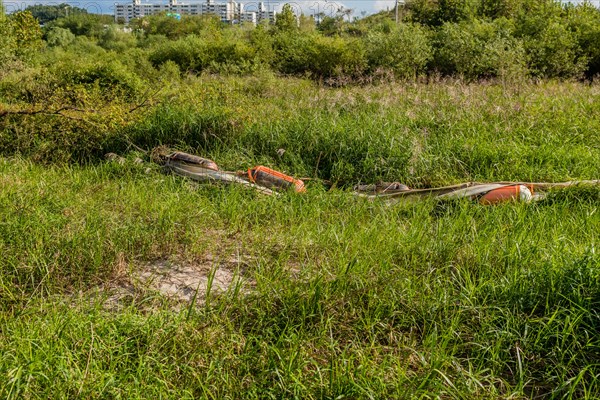 Debris laying in tall grass after flooding caused by monsoon rains with apartment buildings in