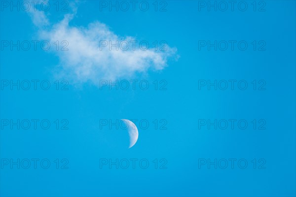 The crescent of the waxing moon in the second quarter shines during the day in a clear blue sky