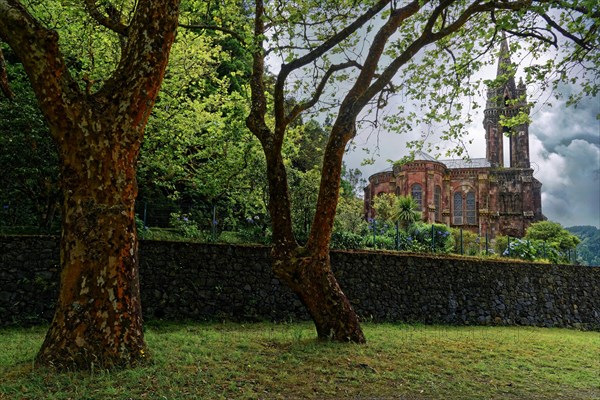 Hidden Gothic church Capela de Nossa Senhora das Vitorias behind trees and an old stone wall in a