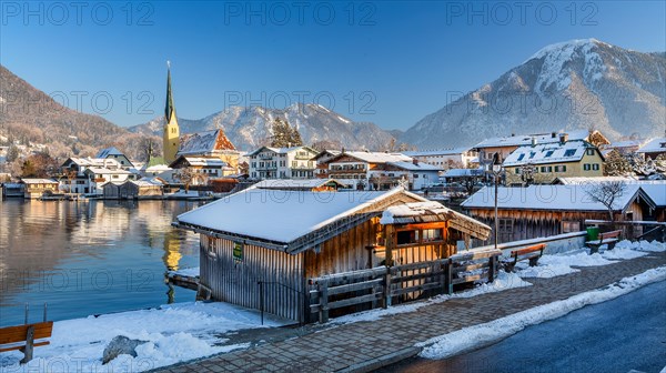 Snowy winter view of Malerwinkel with boathouses, parish church and Wallberg 1722m, Rottach-Egern,