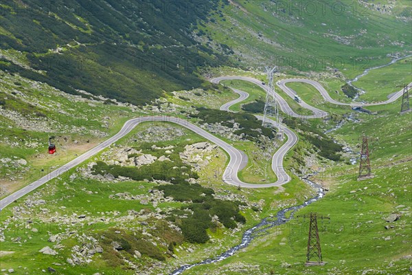 A serpentine road winds through the mountain landscape with views of electricity pylons, Balea