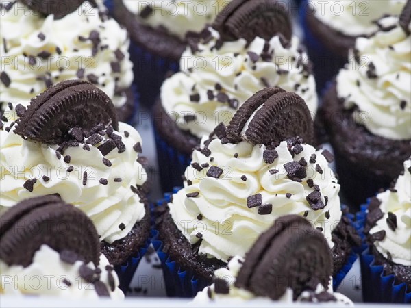 Close-up of a large group chocolate cupcakes with white cream frosting and dark chocolate cookie